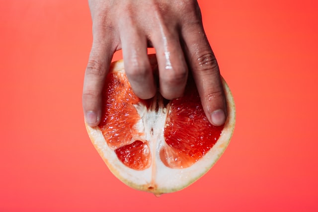 Person holding a red pomelo fruit. Two fingers are pushed inside suggestively.