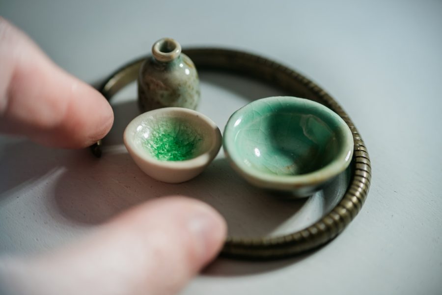 person holding miniature silver and teal stone cups
