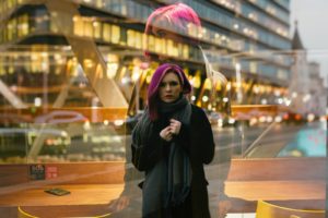 woman in black coat standing near glass wall, her reflection doubled in different sizes