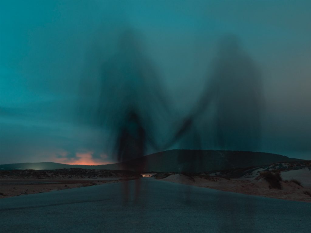 ghost-like long exposure of two figures holding hands and walking down a dark road