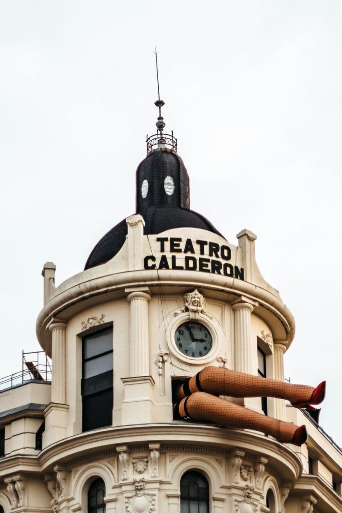 Enormous legs in fishnet stockings and red heels sticking out of a window at Teatro Calderon, Madrid during day